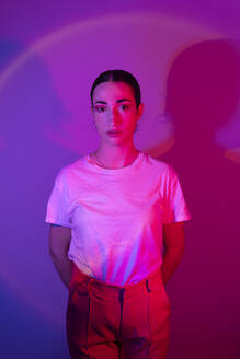 Junge Frau mit Händen hinter dem Rücken in Neonbeleuchtung gegen Gradient Hintergrund - EGHF00868