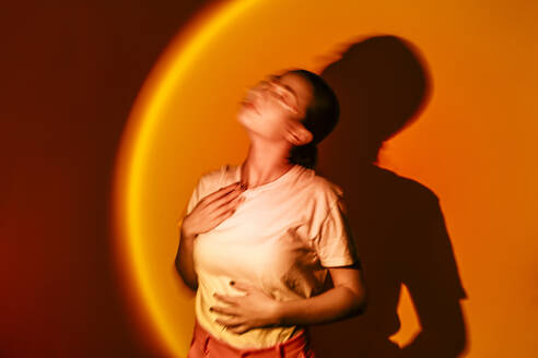 Junge Frau in Neonbeleuchtung vor orangefarbenem Hintergrund - EGHF00872