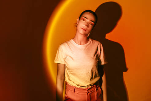 Young woman standing in neon lighting against orange background - EGHF00873