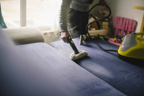Haushälterin reinigt Sofa mit Staubsauger zu Hause - ASHF00081