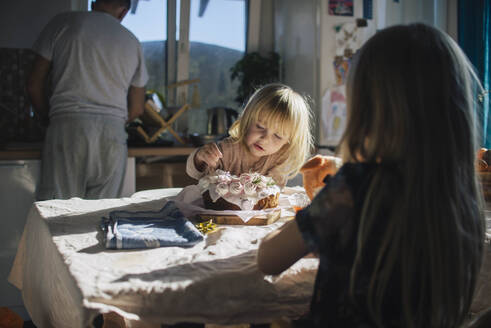 Mädchen isst Kuchen in der Nähe der Schwester in der Küche zu Hause - ASHF00086
