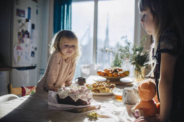 Schwestern lehnen sich an und betrachten den Kuchen auf dem Küchentisch - ASHF00088