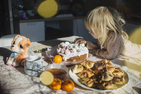 Mädchen mit blondem Haar dekoriert Kuchen auf einem Tisch zu Hause - ASHF00091