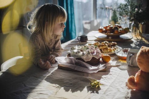 Mädchen starrt auf Kuchen auf dem Esstisch zu Hause - ASHF00095