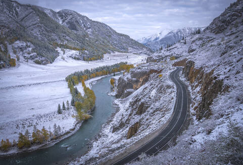 Aerial view of a road along the river crossing the mountain range in winter with snow on the Altai Mountain range, Gorny Altai republic, Russia. - AAEF26124