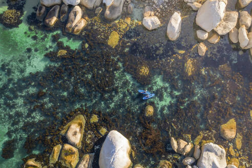 Luftaufnahme von zwei Paddelboardern im klaren türkisfarbenen Wasser des Ozeans, umgeben von Seetang und Felsbrocken an einem heißen Sommertag, Kapstadt, Westkap, Südafrika. - AAEF26505