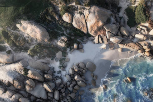 Luftaufnahme einer Bucht, eines abgelegenen Strandes, umgeben von hoch aufragenden Felsbrocken und blauem Meerwasser, das auf den Strand rollt, Kapstadt, Westkap, Südafrika. - AAEF26512