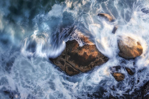 Aerial view of a boulder in the ocean with large waves crashing around it, using a long exposure to capture the motion of the waves, Cape Town, Western Cape, South Africa. - AAEF26524