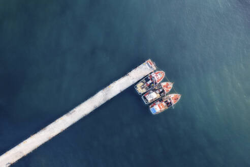 Aerial view of three red fishing boats docked in the harbour with blue water, Cape Town, Western Cape, South Africa. - AAEF26534