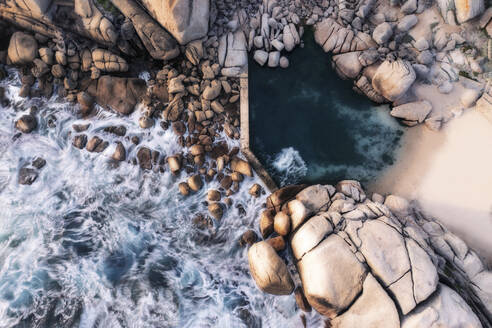Luftaufnahme eines Gezeiten-Felsbeckens, aufgenommen mit einer langen Belichtungszeit, die die Wellen zeigt, die auf die Felsen prallen und in das Becken fließen, Kapstadt, Westkap, Südafrika. - AAEF26539