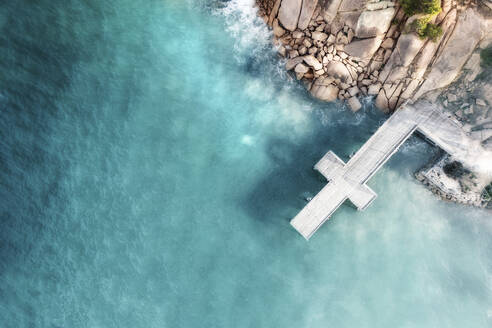 Aerial view of a cross-shaped jetty over blue water with granite rocks and boulders in the image, Port Elliot, South Australia, Australia. - AAEF26551