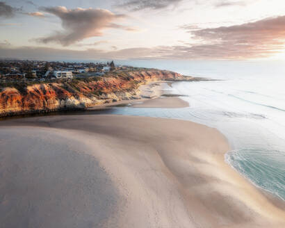 Aerial view of Southport Beach and cliffs at sunset, with pink clouds and a colourful umbrella on the beach Onkaparinga, South Australia, Australia. - AAEF26552