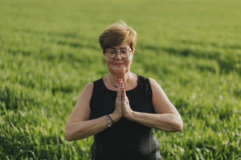 Ältere Frau mit geschlossenen Augen übt Yoga auf einer Wiese - DMGF01273