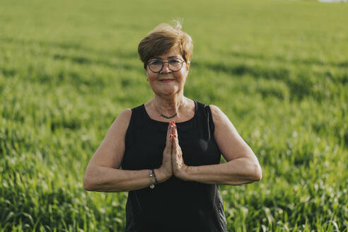 Ältere Frau mit Brille übt Yoga auf einer Wiese - DMGF01274