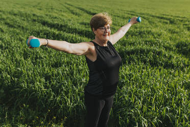 Senior woman exercising with dumbbells in meadow - DMGF01275