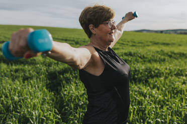 Retired senior woman exercising with dumbbells in meadow - DMGF01276