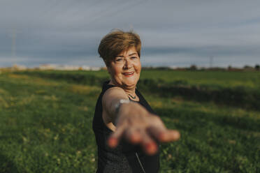 Smiling senior woman exercising with arms outstretched in meadow - DMGF01280