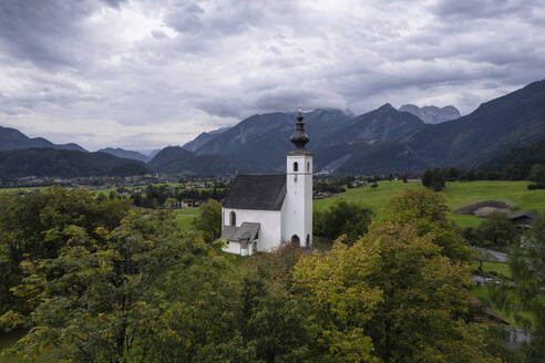 Aerial drone view of Wallfahrtskirche St. Nikolaus with Golling an der Salzach in background at cloudy day, Golling an der Salzach, Salzburg, Austria. - AAEF26785