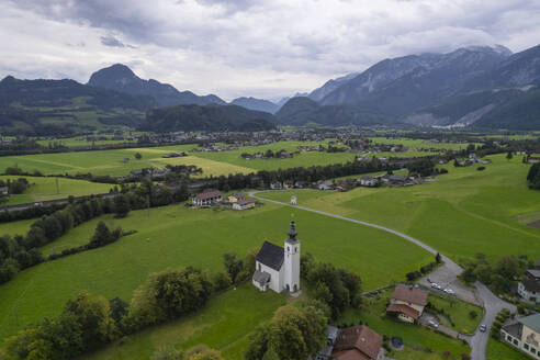 Aerial drone view of Wallfahrtskirche St. Nikolaus with Golling an der Salzach in background at cloudy day, Golling an der Salzach, Salzburg, Austria. - AAEF26787