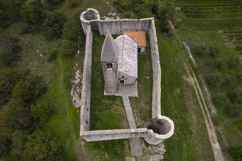 Drohnenaufnahme der Kirche der Heiligen Dreifaltigkeit (Cerkev Sv. Trojice), umgeben von einer Mauer, Hrastovlje, Koper, Slowenien. - AAEF26821