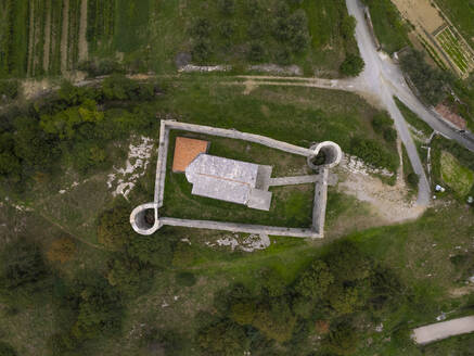 Luftaufnahme der Kirche der Heiligen Dreifaltigkeit (Cerkev Sv. Trojice) von oben, umgeben von einer Mauer, Hrastovlje, Koper, Slowenien. - AAEF26822