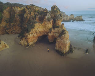 Aerial view of a person on Praia dos Tres Irmaos beach with beautiful rock formations and algae, Algarve, Portugal. - AAEF26847