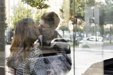 Young couple kissing seen through glass window of real estate office - MASF43557