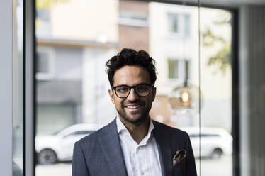 Portrait of smiling male real estate against glass door in office - MASF43565