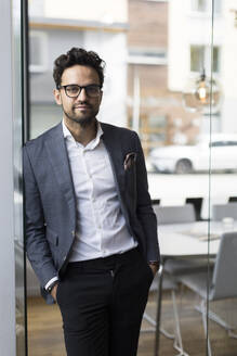 Portrait of confident male real estate agent standing with hands in pockets at office - MASF43567