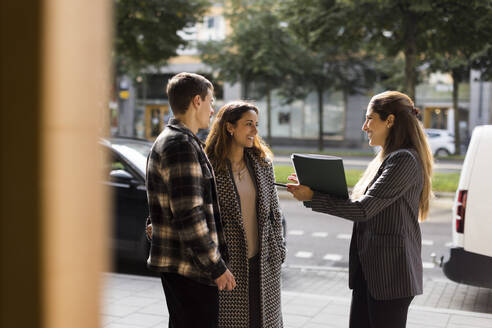 Smiling saleswoman talking with couple while standing at street - MASF43578