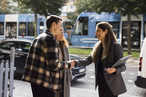 Smiling man doing handshake with female real estate agent while standing at street - MASF43579