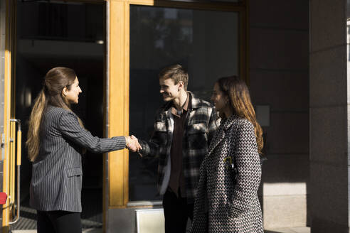 Happy couple shaking hand with female real estate agent in front of apartment - MASF43580