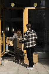 Multiracial couple carrying boxes while walking in apartment building - MASF43586