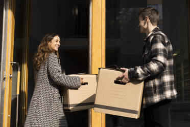 Multiracial couple assisting each other while carrying boxes during relocation of house - MASF43588