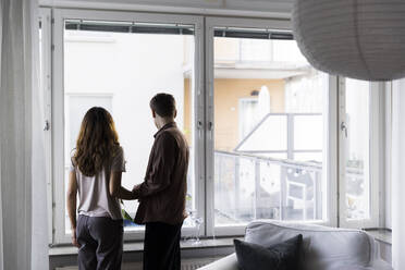 Couple looking through window while standing in new home - MASF43594