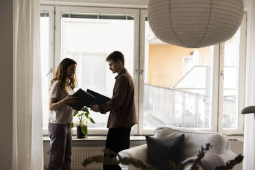 Couple holding agreement files while standing near window at new home - MASF43595