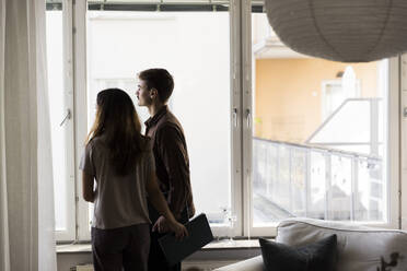 Multiracial couple looking through window while standing at new home - MASF43596