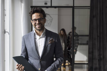 Portrait of happy male real estate agent holding folder at home - MASF43603