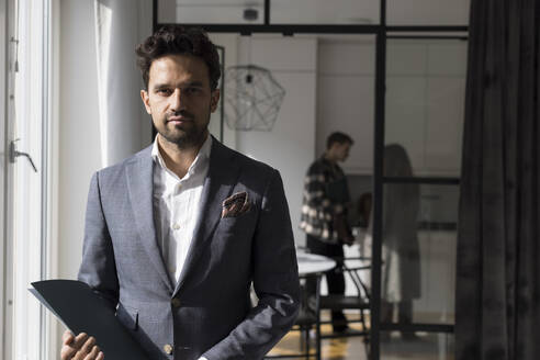 Portrait of confident salesman holding folder while standing at home - MASF43604