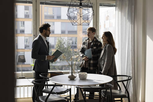 Salesman taking with couple while standing near table during meeting at home - MASF43607