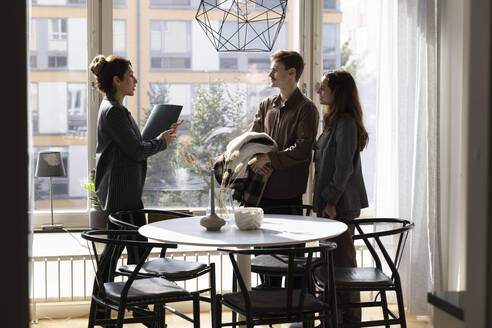 Female real estate agent discussing with customers while standing at new home - MASF43611