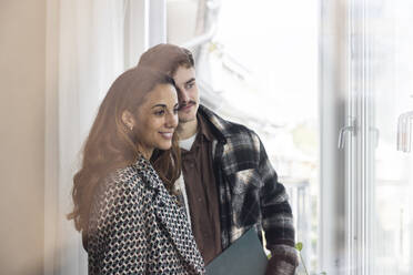 Smiling multiracial couple looking through window in balcony while exploring new house - MASF43616