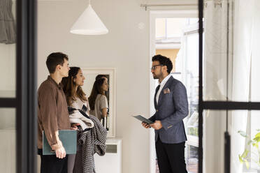 Salesman discussing with male and female clients while standing at home - MASF43620