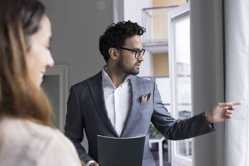 Male real estate agent pointing while talking with female client at home - MASF43622