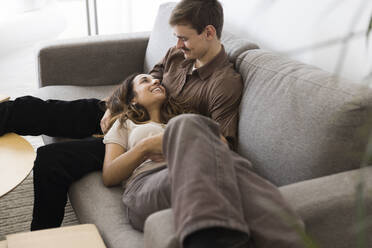 Smiling woman lying down on boyfriend's lap sitting on sofa at home - MASF43627
