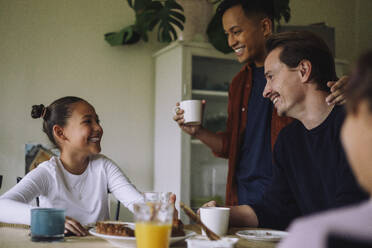 Happy gay couple with daughter having breakfast while sitting at dining table in home - MASF43631