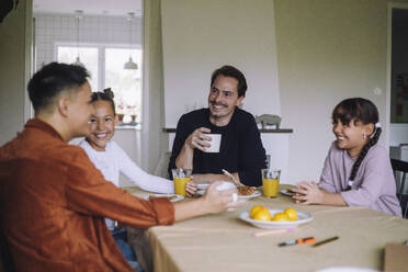 Happy gay couple spending leisure time with daughters while having breakfast at dining table in home - MASF43633