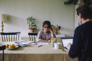 Girl studying with father using laptop while sitting at dining table in home - MASF43636