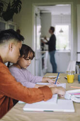 Gay man assisting daughter doing homework while sitting at dining table in home - MASF43638