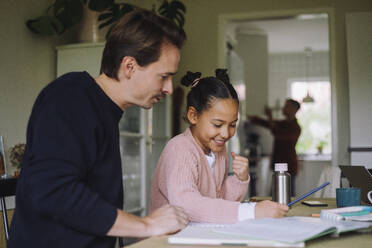 Father sitting next to excited daughter doing homework at home - MASF43641